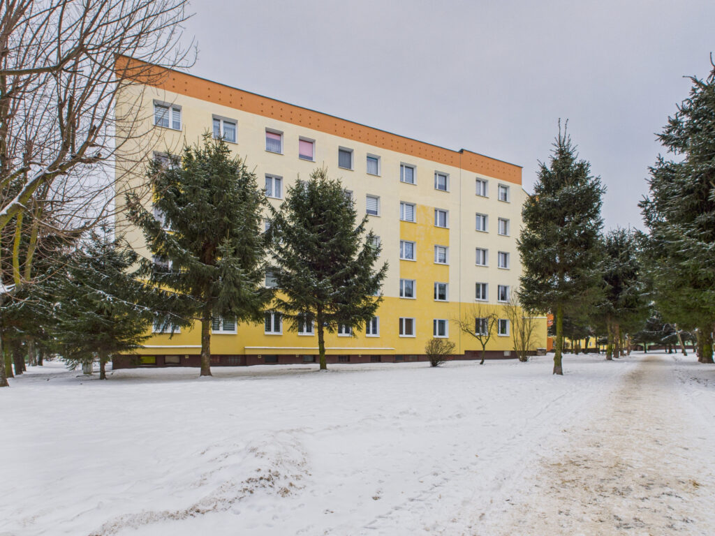 Blok mieszkalny zimą, otoczony zielenią.