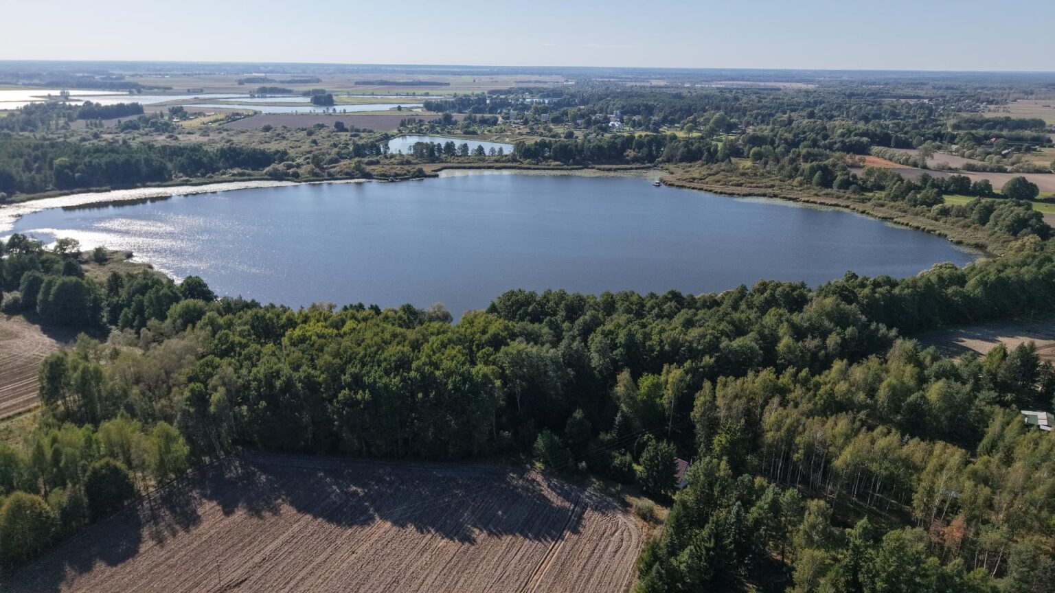 Widok jeziora otoczonego lasami i polami