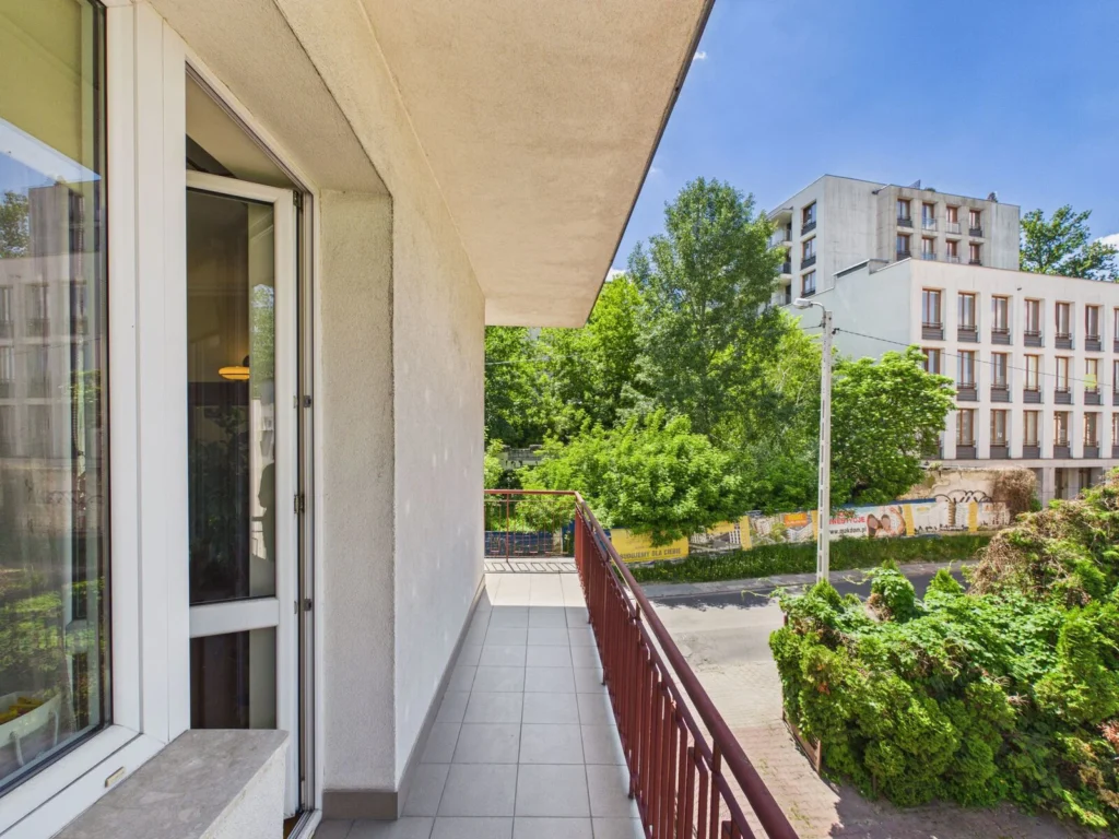 Balkon mieszkania z widokiem na drzewa i budynek