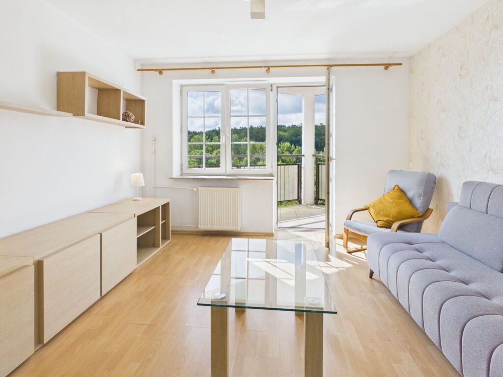 Jasny salon z balkonem, szarą sofą i fotelem