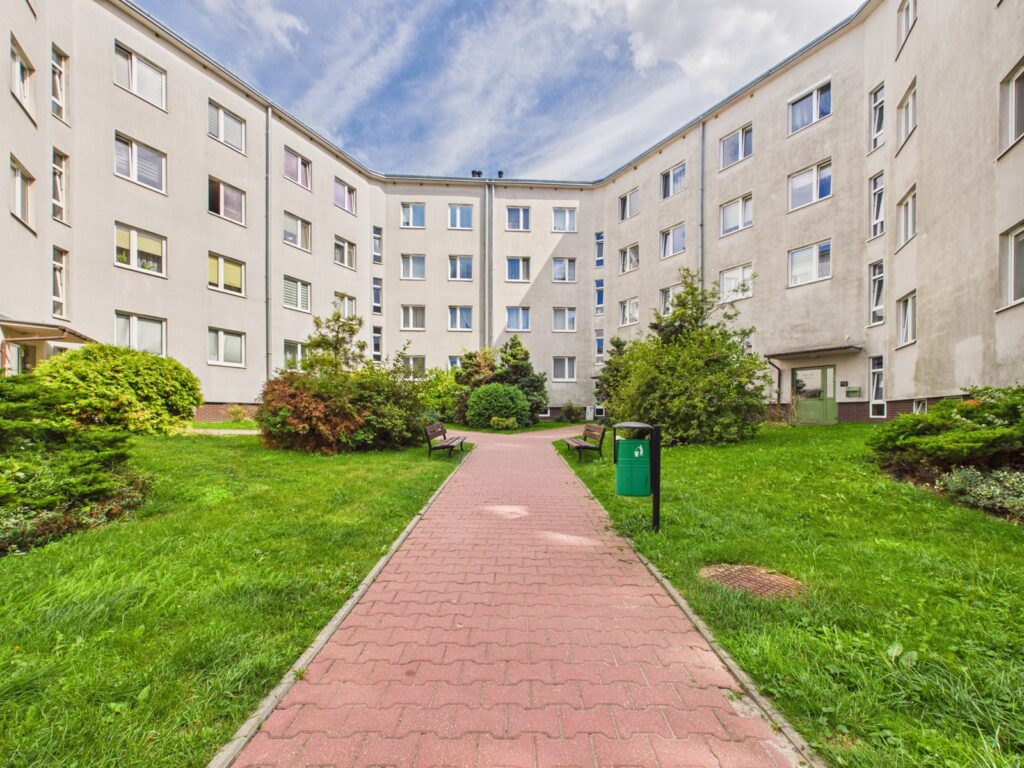 Dziedziniec osiedla z chodnikiem, ławkami i zielenią