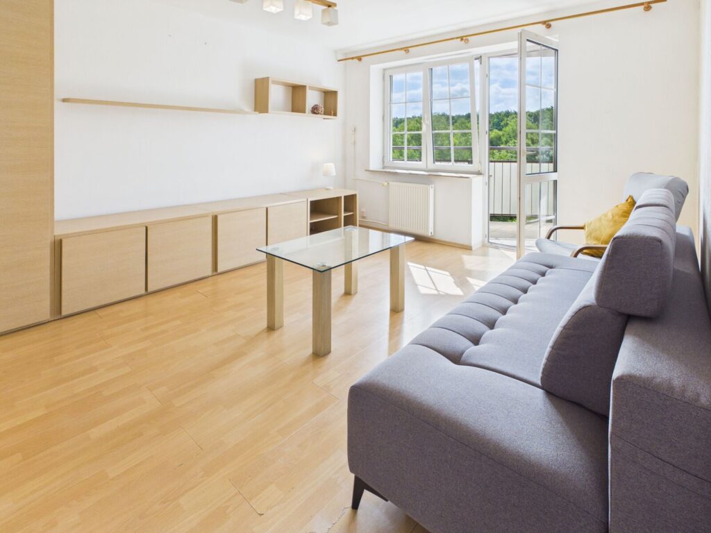 Jasny salon z szarą sofą i balkonem