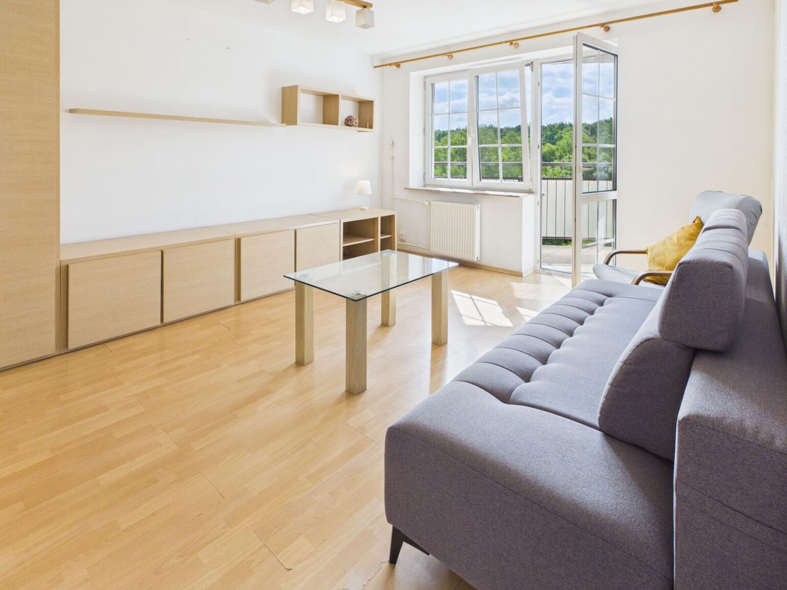 Jasny salon z szarą sofą i balkonem