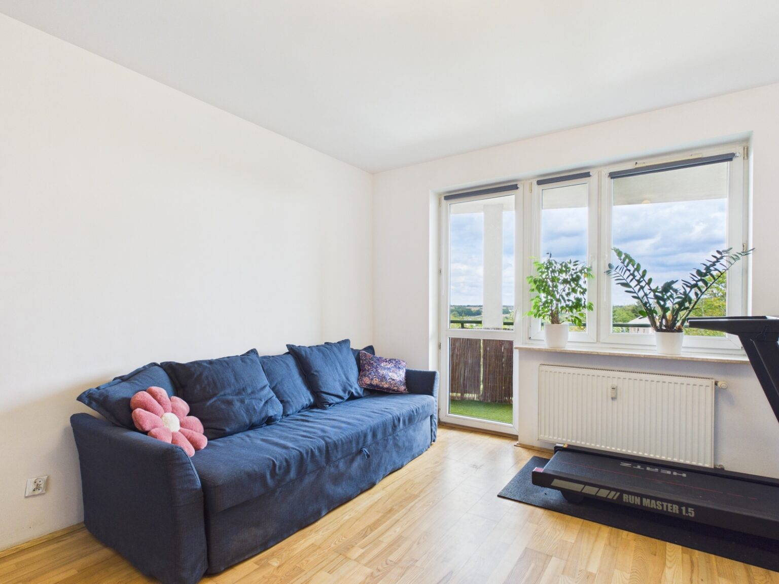 Jasny salon z granatową sofą, bieżnią i balkonem
