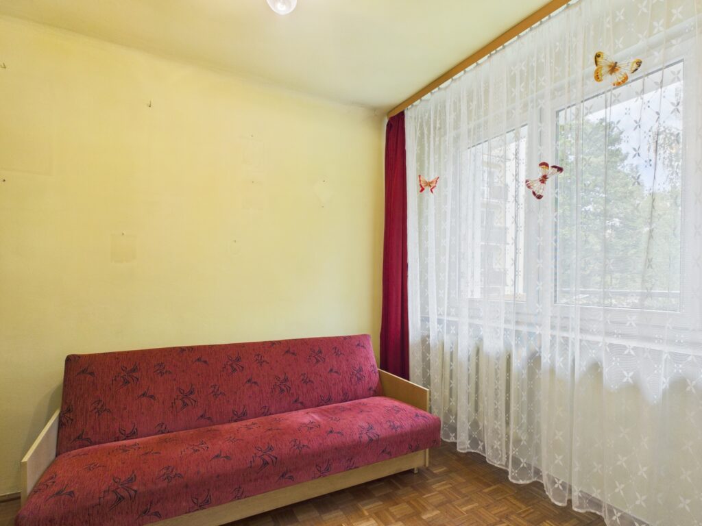 Czerwony tapczan przy dużym oknie z firanami