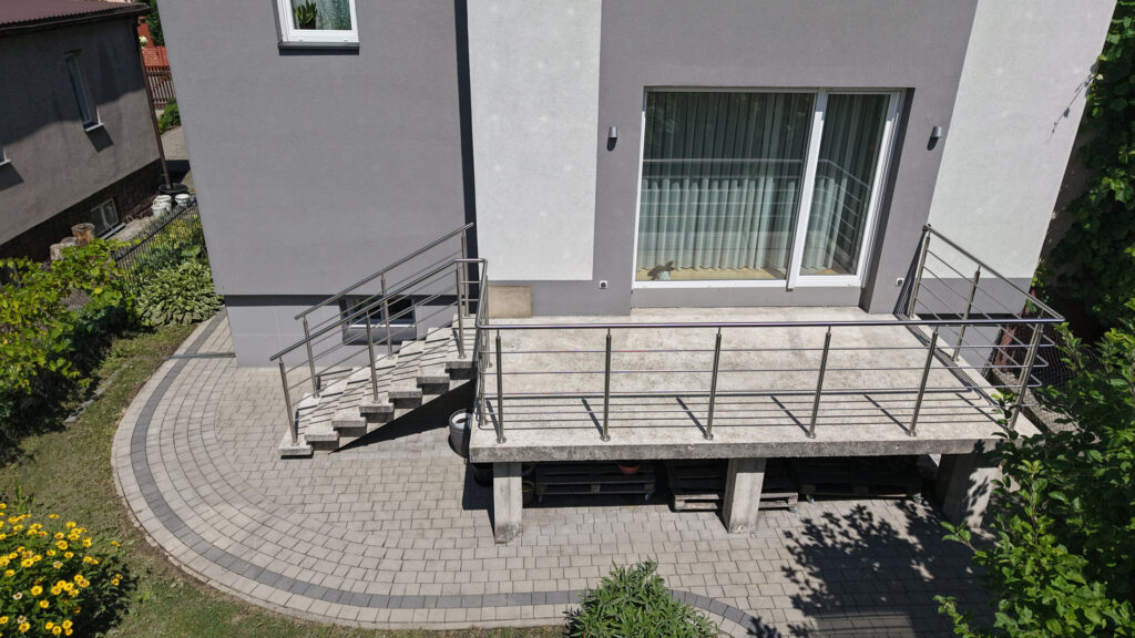 Taras domu z metalową balustradą i brukowanym podjazdem