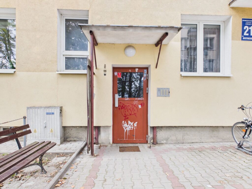Wejście do kamienicy z czerwonymi drzwiami i daszkiem