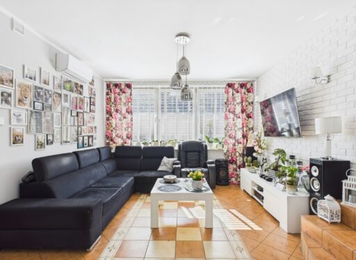 Jasny salon z czarną sofą i kwiatowymi zasłonami